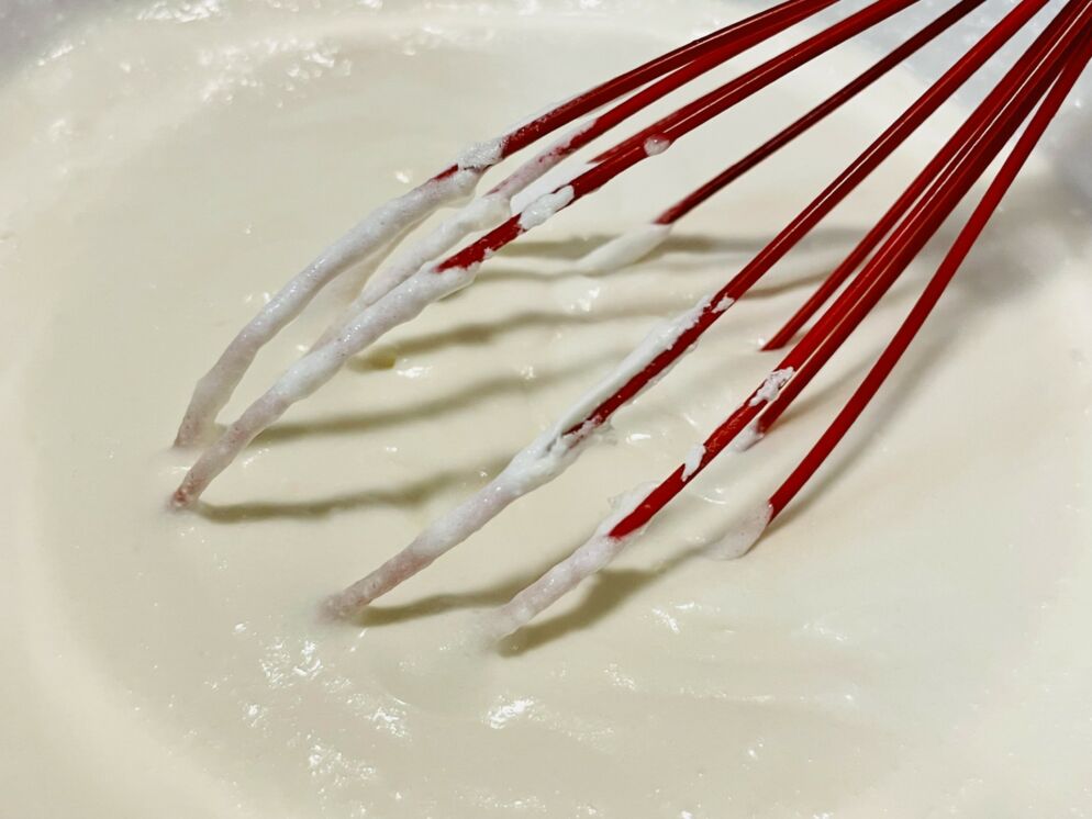 A red whisk stirs a thick, white mixture. 
