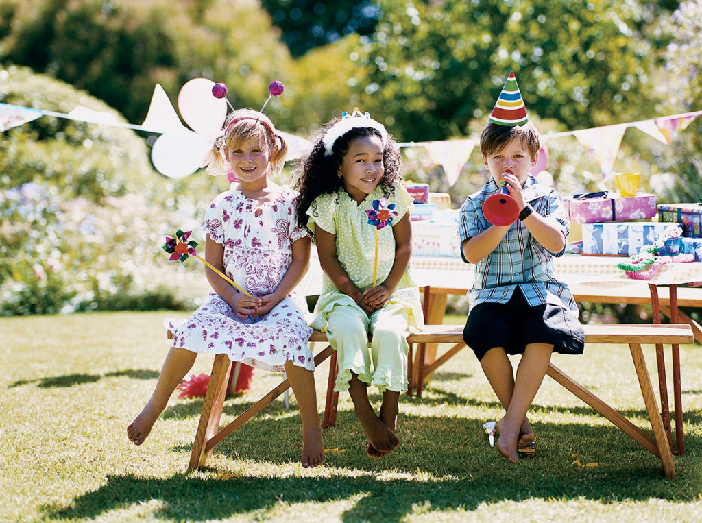 Two Girls and One Boy Sitting at a Garden Table at a Birthday Party