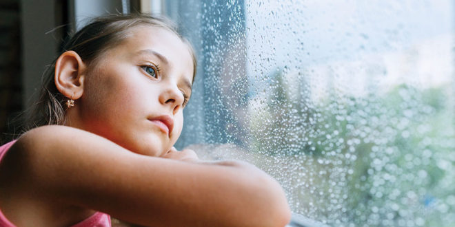 Little sad girl pensive looking through the window glass with a lot of raindrops. Sadness childhood concept image.