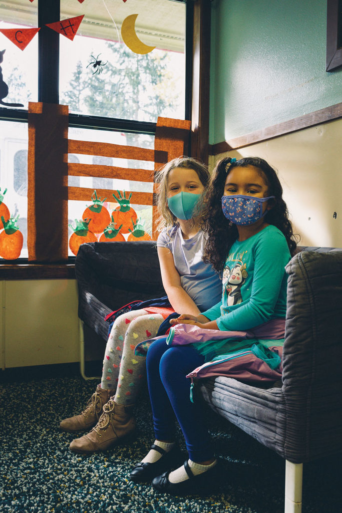 Two girls with masks on sit together
