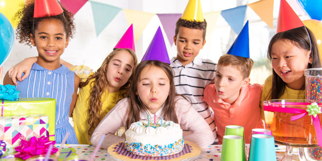 Girl blows out candles on a birthday cake surrounded by friends