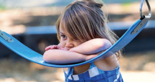 Sad little girl leans on swing