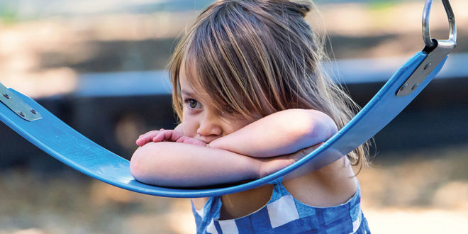 Sad little girl leans on swing