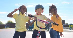 A group of 3 children pose next to a bicycle.