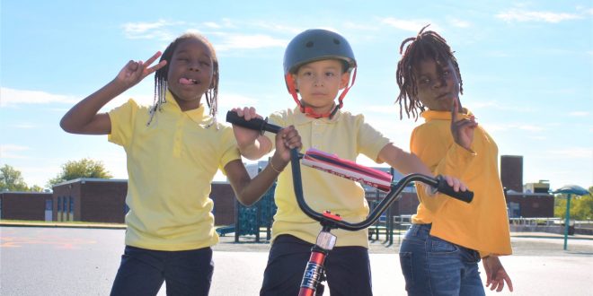 A group of 3 children pose next to a bicycle.