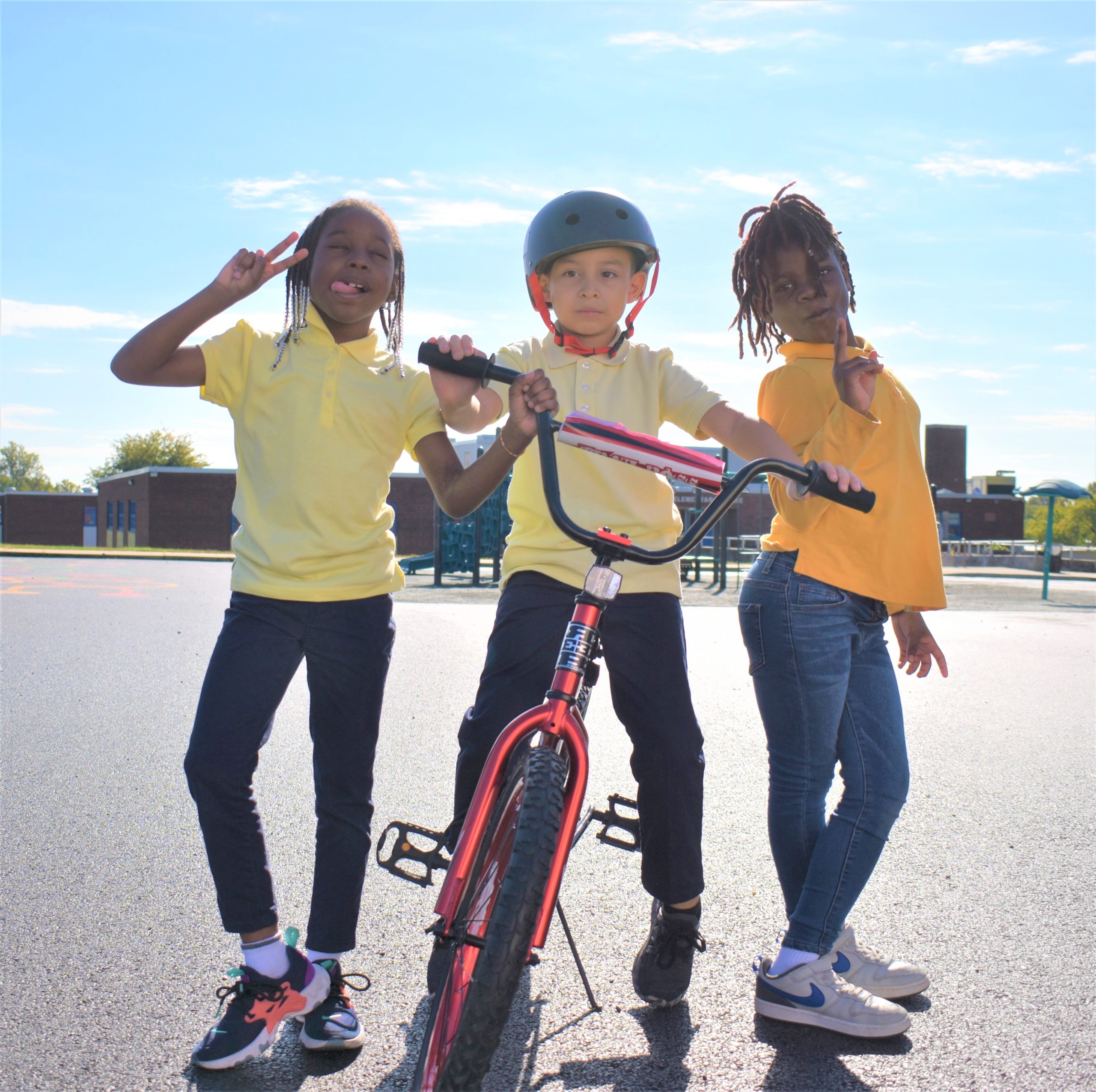A group of 3 children pose next to a bicycle. 