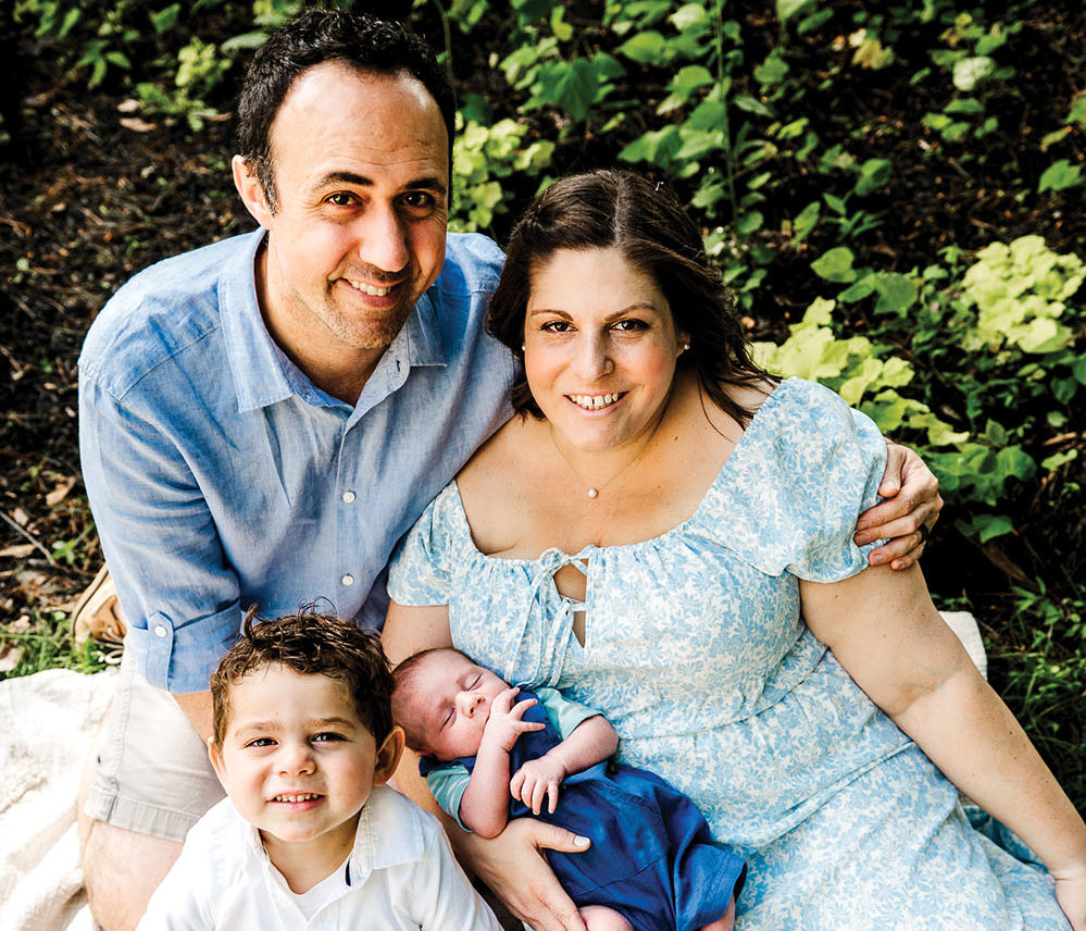 Melissa Seltzer and her husband smile in blue clothing while holding their sons.