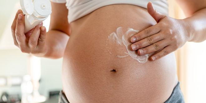 A pregnant woman applies lotion to her stomach.