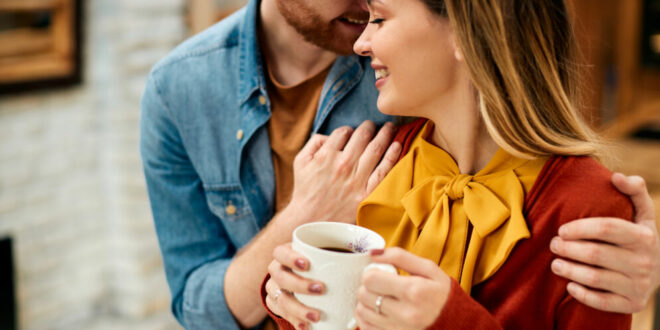 Young smiling couple enjoying in their love while having cup of coffee at home.