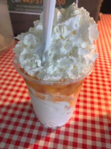 A close-up of the Maryland State Fair's peach sundae, layered with vanilla ice cream, fresh peaches and whipped cream. A spoon anchored in the sundae cup sticks out the top.