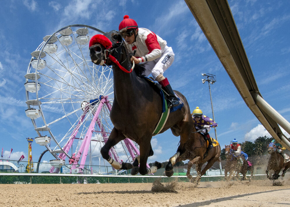 Photo of a person riding a horse against a sunny blue sky and a Ferris wheel in the background.