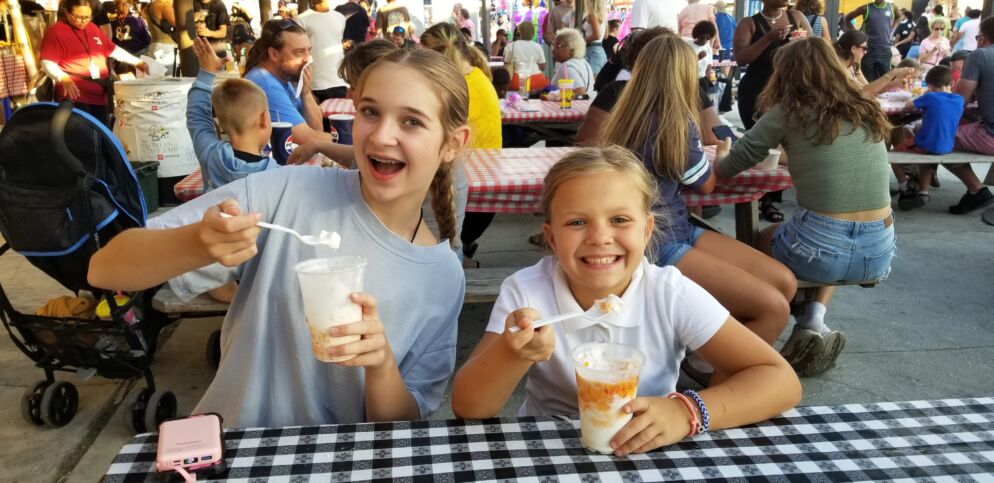 Two girls enjoy treats at the Maryland State Fair while seated at picnic tables.