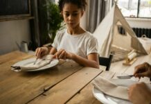 Towson’s International School of Protocol Brings Etiquette to Roland Park Young Black girl watches an adult use cutlery at a place setting as she tries to imitate.