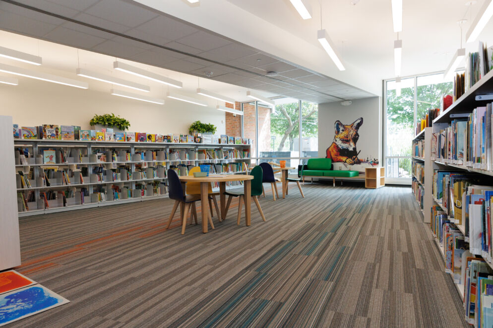 A brightly lit room with neat carpet, tables and chairs and bookshelves. There is a mural of a fox on the wall. 