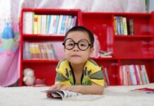 BCPL Supports Freedom to Read During Banned Books Week Little Asian boy with black-rimmed glasses looks ahead, lying on the floor holding the page of an open book.