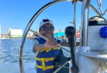 A Black girl wearing a blue life jacket with yellow ties holds the wheel of a boat out on the water. Alexis Snyder, 13, is the subject of the photo. The teen has dealt with kidney issues and is the National Kidney Foundation Ambassador for 2024. She is speaking at the Maryland Kidney Walk Oct. 6, 2024.