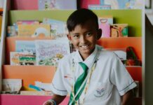 New Leadership for Enoch Pratt Free Library A male student sits in front of a book stand full of books, with one open to read on his lap.