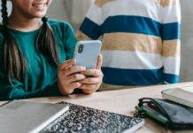 What to Know About Instagram Teen Accounts Stock photo of a tween girl smiling as she uses a cell phone at a table.