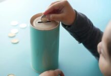 Child puts a coin in a piggy bank; the camera shows the back of the child putting the money in