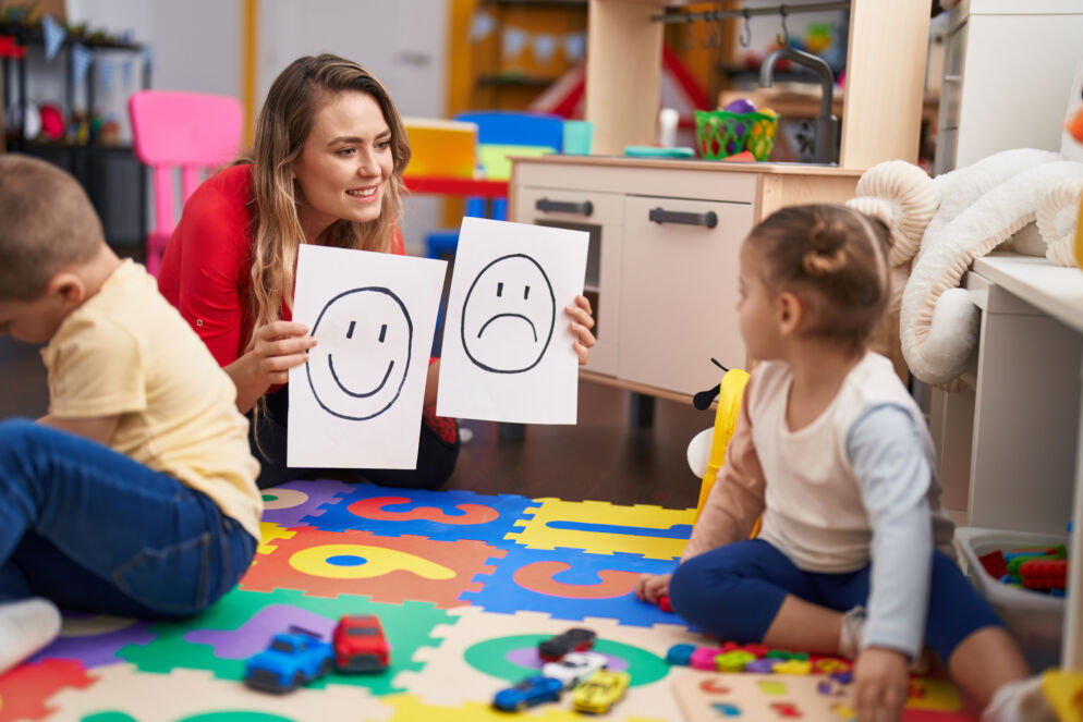 Teacher with boy and girl sitting on table having emotion therapy at kindergarten