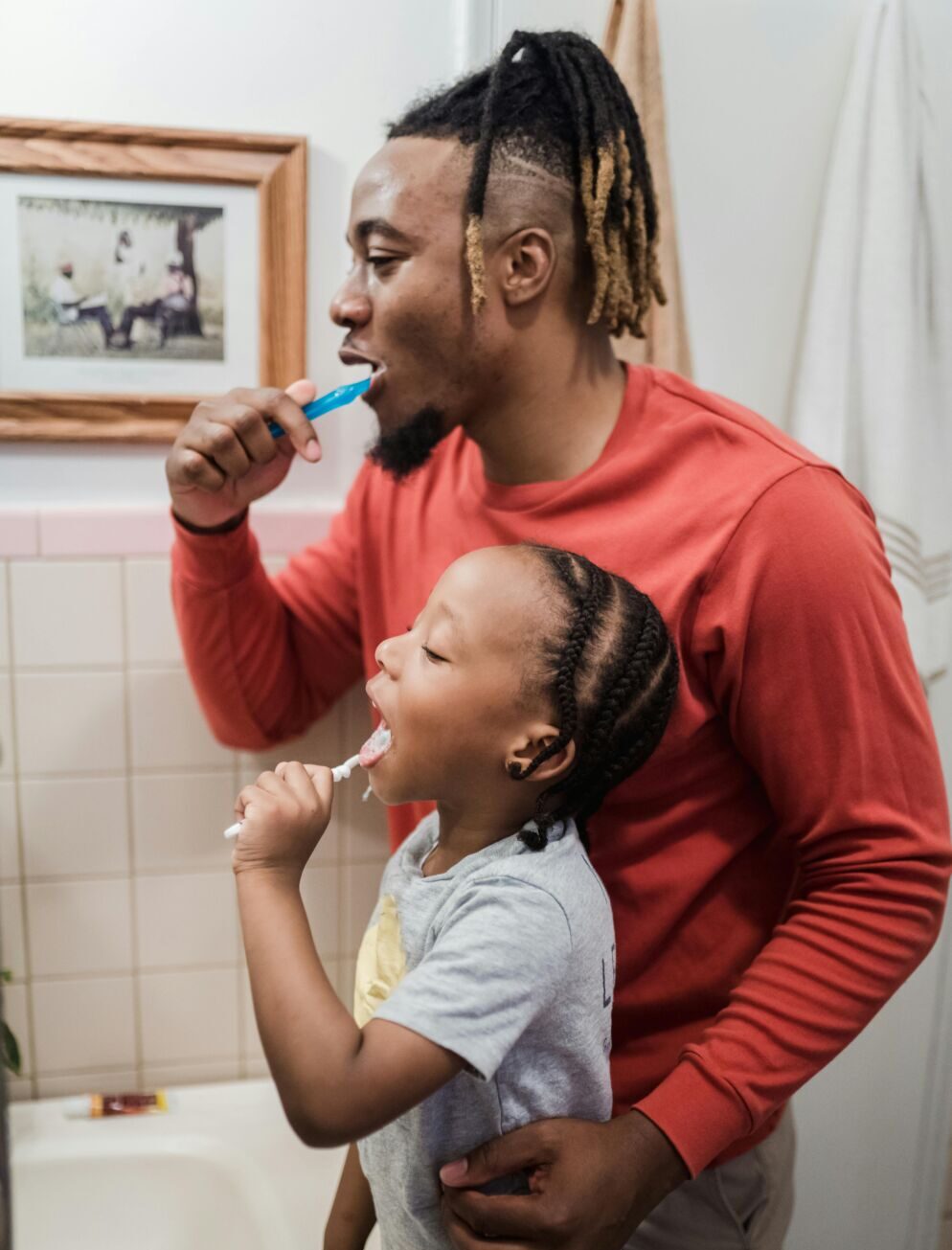 A child and their father brushing their teeth in front of a mirror