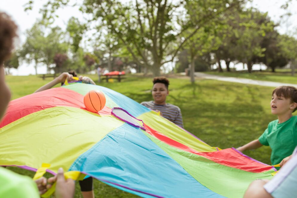 Kids at a summer camp playing with a parachute with balls on it 