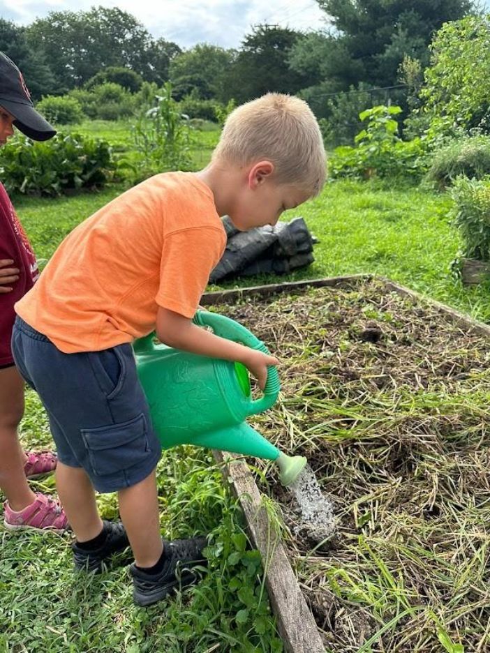A young boy watering plants at Adamah Adventure Camp