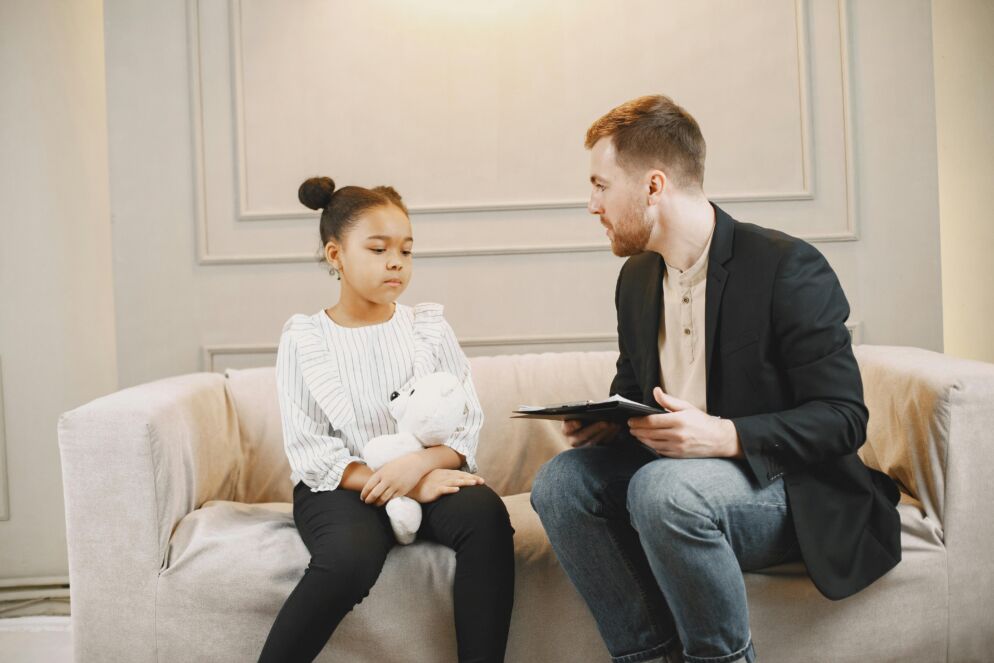 A therapist speaking to a child holding a teddy bear