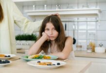 Girl sitting at a table with a plate of food, looking grumpy