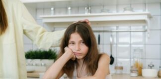 Girl sitting at a table with a plate of food, looking grumpy