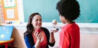 A teacher receives an apple and a trophy that says "best teacher" from a student
