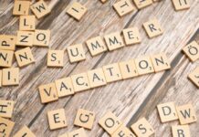 Scrabble tiles spell out "Summer Vacation" on a wooden background.