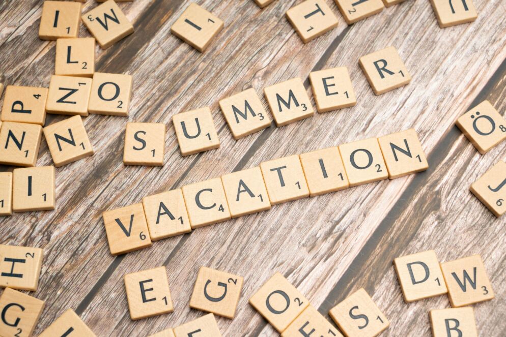 Scrabble tiles spell out "Summer Vacation" on a wooden background.