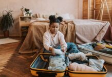 Only the Essentials: Summer Camp Packing Tips A child sits on the floor, looking pensive as she packs her suitcase. This photo represents packing for summer camp or a summer trip.