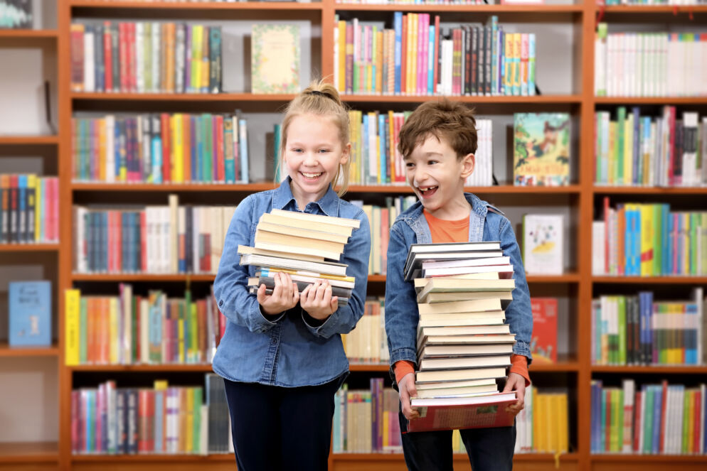 Kids standing in front of a bookshelf holding stacks of books