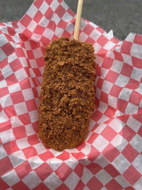 Biscoff cookie butter crumbles cover frozen cheesecake on a stick on red and white checkered paper at the Maryland State Fair