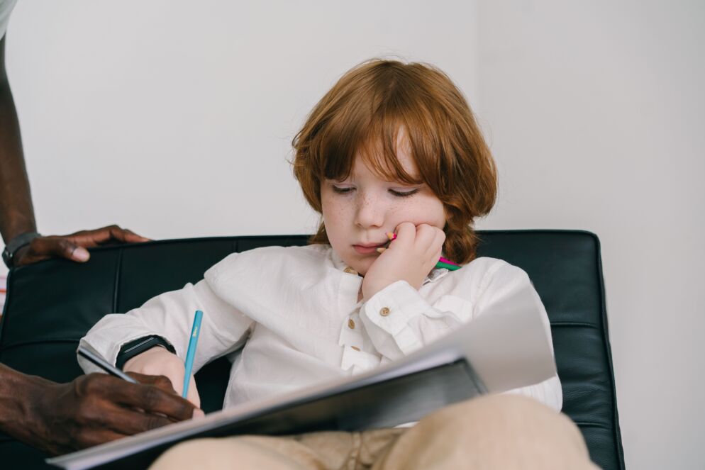 Child writing in a notebook with colored pencils